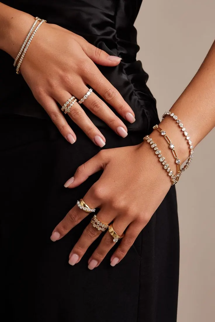 Hands wearing stacked gold and diamond rings and bracelets